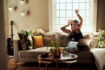 Eine Frau auf dem Sofa mit einem Laptop, die sich über die Unterschiede zwischen Hausrat- und Wohngebäudeversicherung informiert