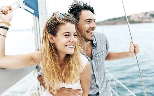 Ein junges Paar fährt im Urlaub auf einem Segelboot und ist mit einer Reiseunfallversicherung abgesichert.