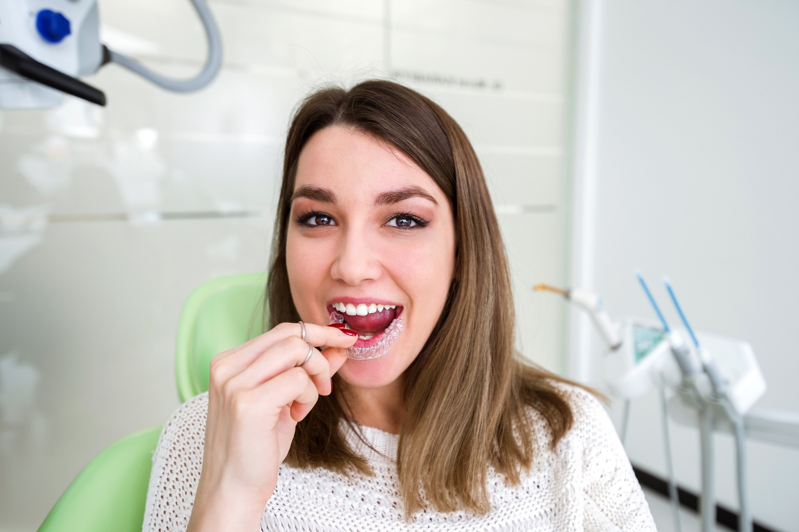 Eine Frau sitzt auf einem Zahnarztstuhl und hält ihre Zahnschiene in der Hand.