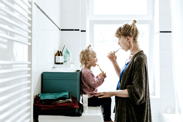 Eine junge Mutter bringt ihrer Tochter das Zähneputzen bei.