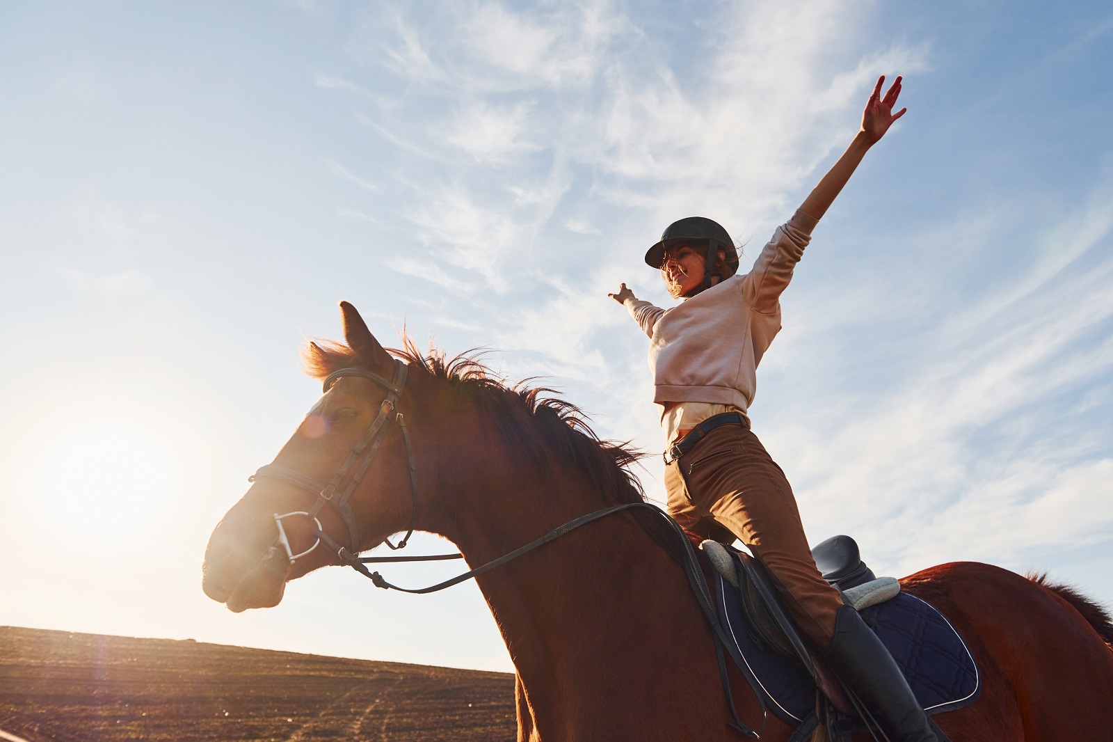 Junge Frau im Schutzhut mit ihrem Pferd auf dem landwirtschaftlichen Feld bei sonnigen Tageszeiten.