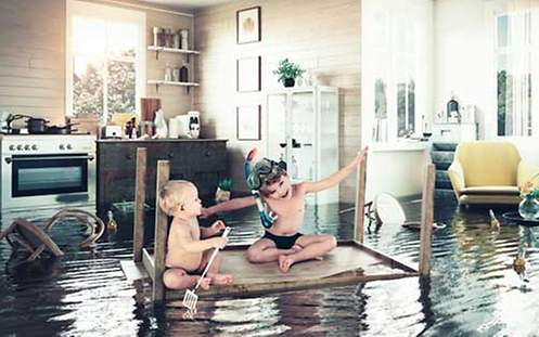 Kinder schwimmen auf einem Tisch durch eine überflutete Wohnung.