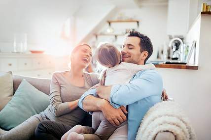 Eine Familie sitzt auf der Couch und blickt entspannt in die Zukunft, weil sie gut abgesichert ist.