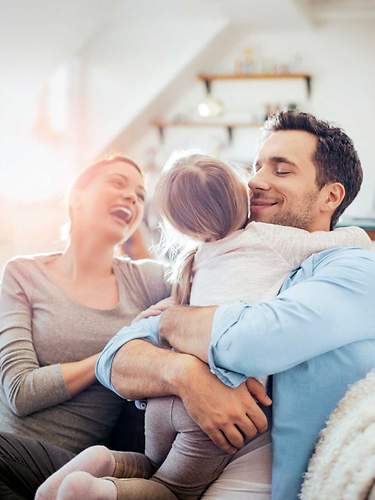 Eine Familie sitzt auf der Couch und blickt entspannt in die Zukunft, weil sie gut abgesichert ist.