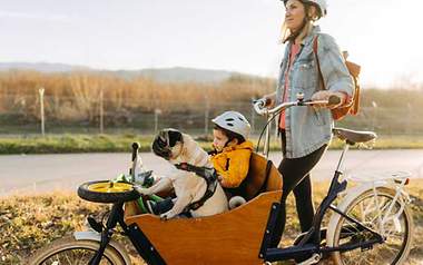 Mit dem Fahrrad Geldbeutel und Umwelt schonen Eine Frau ist mit Ihrem Kind und Hund mit dem Rad unterwegs