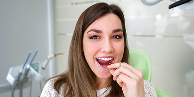 Lachende Frau mit offenem Mund und einer Zahnschiene in der Hand