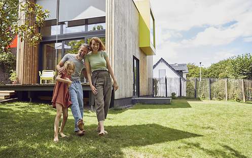 Das Bild zeigt eine Familie vor ihrer Immobilie, die den Kredit für ihr Haus mit einer Risikolebensversicherung abgesichert hat.