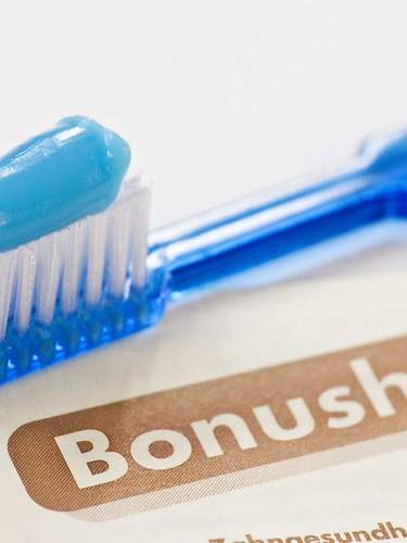 Das Bild zeigt eine Zahnbürste, die auf einem Bonusheft vom Zahnarzt liegt. 