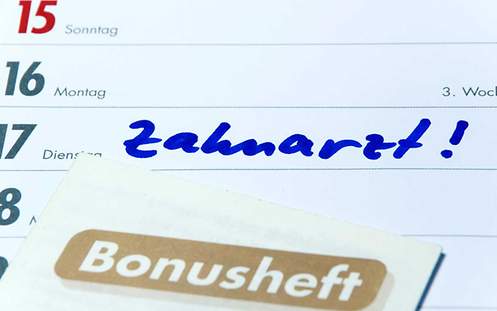 Regelmäßige Vorsorgeuntersuchung Das Bild zeigt einen Terminkalender, in dem ein Zahnarztbesuch vermerkt ist. Auf dem Kalender liegt ein Bonusheft vom Zahnarzt.