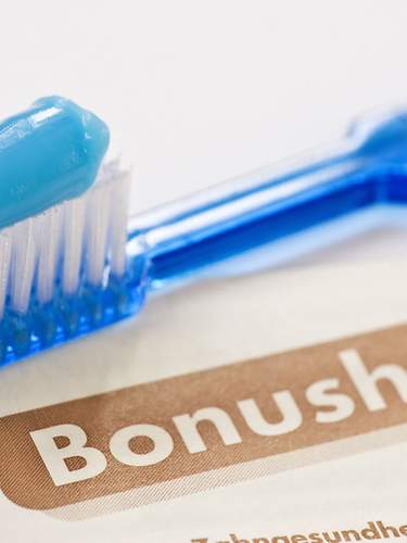 Das Bild zeigt eine Zahnbürste, die auf einem Bonusheft vom Zahnarzt liegt.