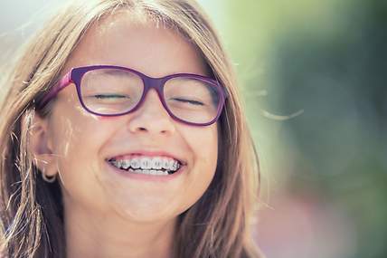 Das Bild zeigt ein lachendes Mädchen, das eine feste Zahnspange trägt.