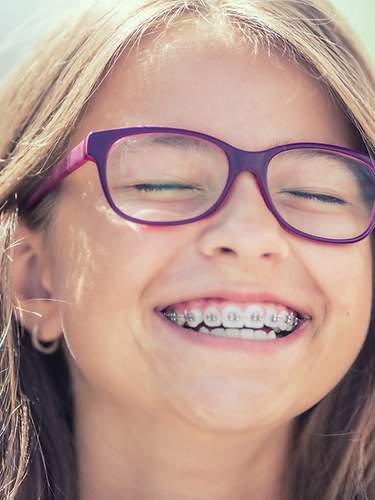 Das Bild zeigt ein lachendes Mädchen, das eine feste Zahnspange trägt.