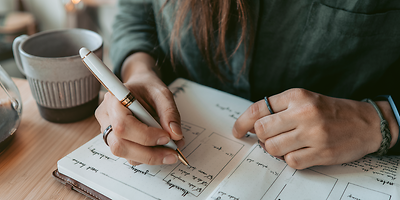 Eine Frau mit langen dunklen Haaren schreibt in ein Buch.