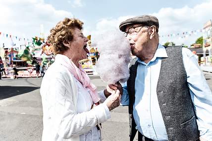 Das Bild zeigt zwei Senioren, die dank der Zahnzusatzversicherung unbeschwert Zuckerwatte genießen können.