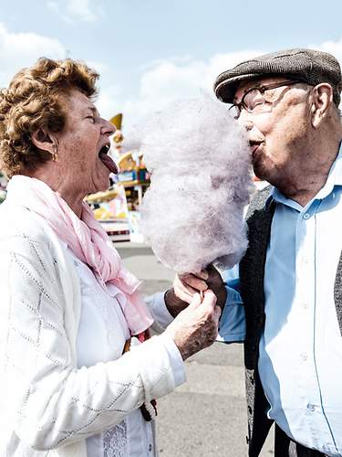 Das Bild zeigt zwei Senioren, die dank der Zahnzusatzversicherung unbeschwert Zuckerwatte genießen können.