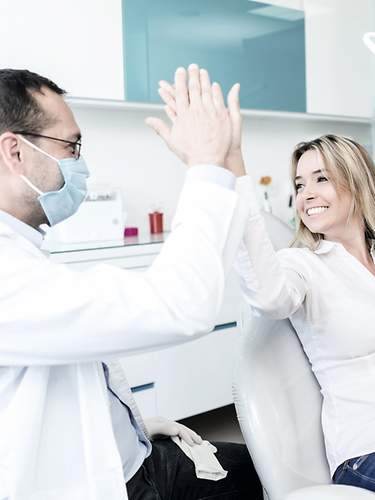 Eine Patientin gibt ihrem Zahnarzt ein High-Five für die Kostenerstattung über die Zahnzusatzversicherung.