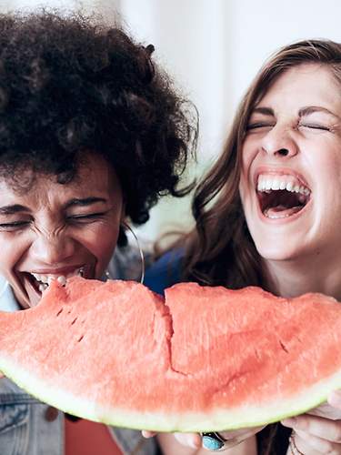 Zwei Frauen essen lachend Wassermelone.