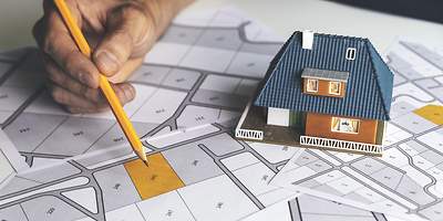 Auf einem Tisch liegen eine Flurkarte und ein Modellhaus, um einen Grundstückskauf vorzubereiten.