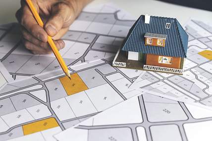 Auf einem Tisch liegen eine Flurkarte und ein Modellhaus, um einen Grundstückskauf vorzubereiten.