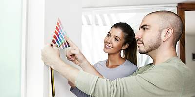 Ein junges Paar sucht sich nach dem Wohnungskauf eine neue Wandfarbe aus. 
