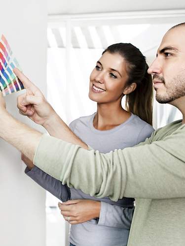 Ein junges Paar sucht sich nach dem Wohnungskauf eine neue Wandfarbe aus. 