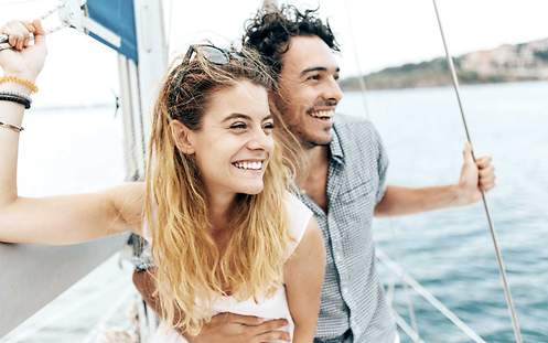 Welche Unfälle deckt die Versicherung auf einer Reise? Ein junges Paar fährt im Urlaub auf einem Segelboot und ist mit einer Reiseunfallversicherung abgesichert.