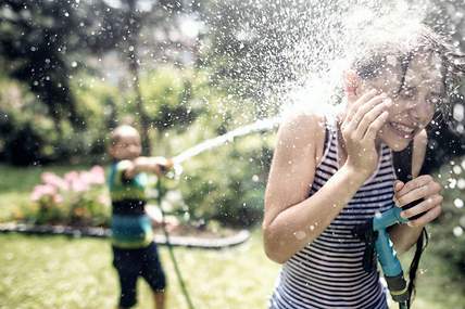 Das Bild zeigt zwei Kinder, die im Garten mit einem Wasserschlauch spielen.