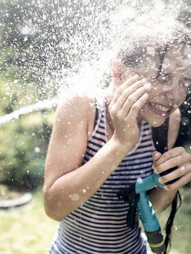 Das Bild zeigt zwei Kinder, die im Garten mit einem Wasserschlauch spielen.