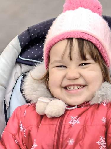 Das Bild zeigt zwei Kinder in einem Kinderwagen, ein Kind ist traurig, das andere fröhlich.