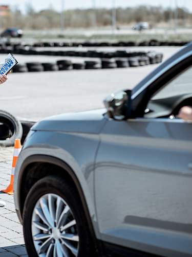 Eine Fahranfängerin zeigt glücklich ihren Autoschlüssel durch das Autofenster.