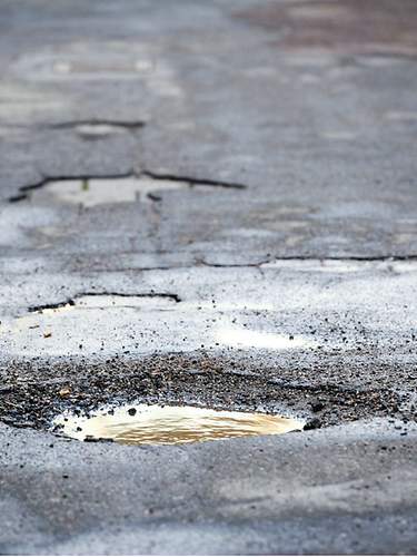 Ein Auto fährt an einem Schlagloch in der Straße vorbei.