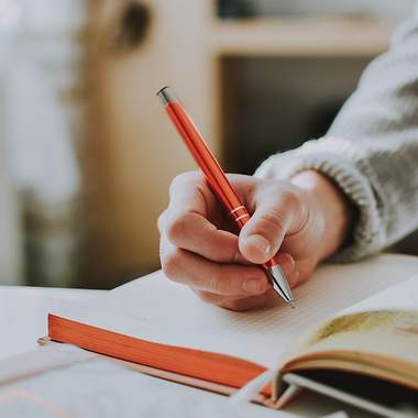 Eine Hand, die einen Stift hält und im Buch schreibt