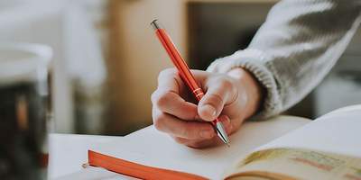 Eine Hand, die einen Stift hält und im Buch schreibt