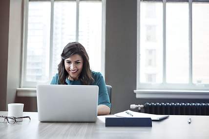 Eine Frau sitzt auf dem Bett und arbeitet an ihrem Laptop.