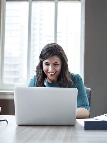 Eine Frau sitzt auf dem Bett und arbeitet an ihrem Laptop.