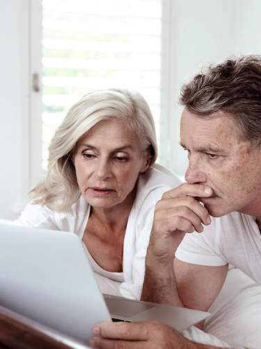 Ein älteres Ehepaar liegt mit Laptop auf dem Bett und denkt über eine Risikolebensversicherung für Rentner nach.