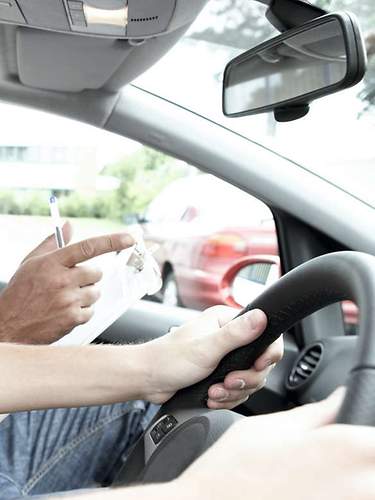 Eine junge Frau sitzt in einem Auto und zeigt stolz ihren Führerschein.