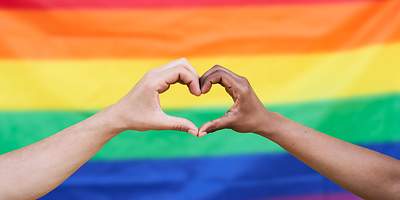 Zwei Hände bilden ein Herz vor einer Regenbogenfarbenflagge
