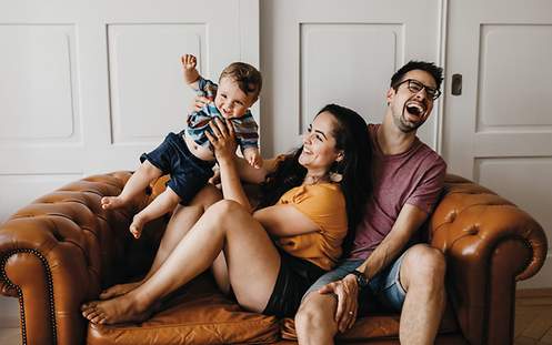 Eine junge Familie spielt glücklich auf dem Sofa und hat sich mit einer Lebensversicherung finanziell abgesichert.