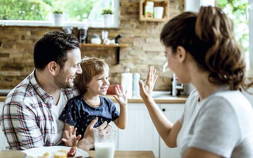 Risikolebensversicherung als Hinterbliebenenschutz Eine Mutter klatscht mit ihrem Kind und dessen Vater am Küchentisch ab.