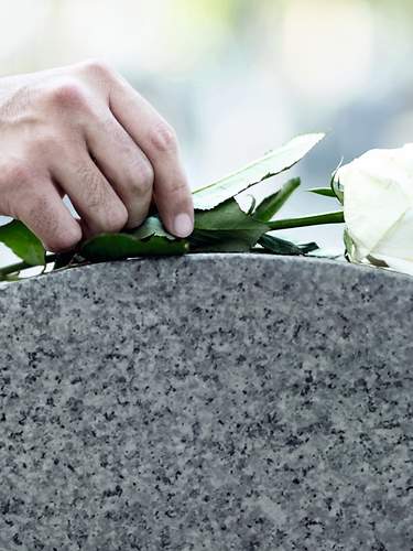 Ein Mann legt eine Rose auf einen Grabstein.