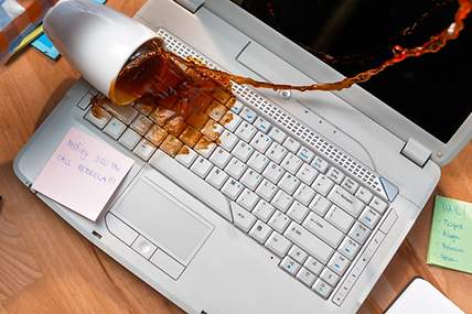 Das Bild zeigt, wie eine Tasse Kaffee über einem Laptop verschüttet wird.