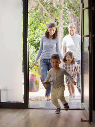 Eine Familie kommt vom Einkauf zurück nach Hause. Die zwei kleinen Kinder rennen ins Haus.