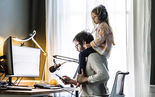 Ein Vater arbeitet im Homeoffice, während seine Tochter auf seinen Schultern sitzt.