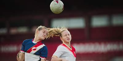 Zwei Fußballspielerinnen springen für einen Kopfball in die Luft 