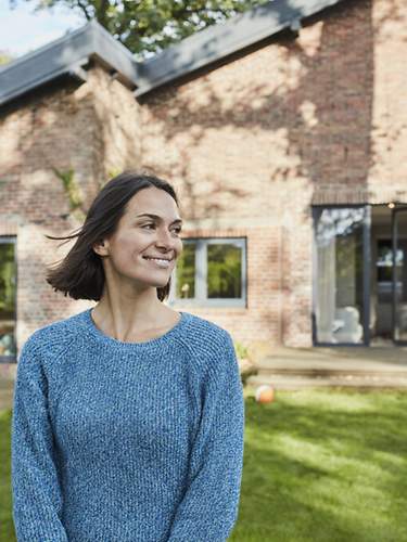 Eine Frau steht lachend im Garten ihres Eigenheims.