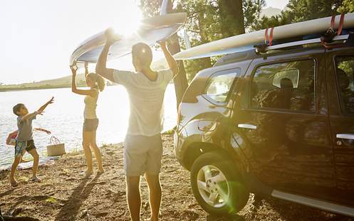 Eine junge Familie ist mit ihrem SUV und Surfbrettern im Gepäck an einen See gefahren.