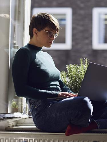 Eine Frau sitzt mit ihrem Laptop am Fenster.