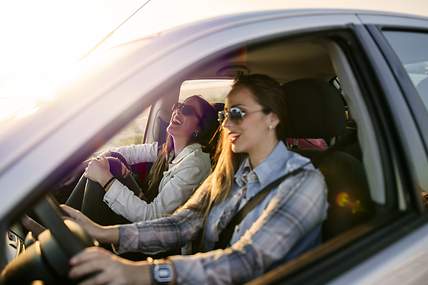 Zwei junge Frauen sitzen lachend in ihrem VW Golf 6.