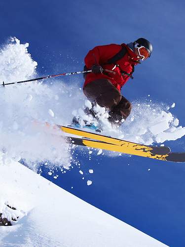 Bei der Abfahrt auf einer Piste springt ein Skifahrer von einem kleinen Felsen.